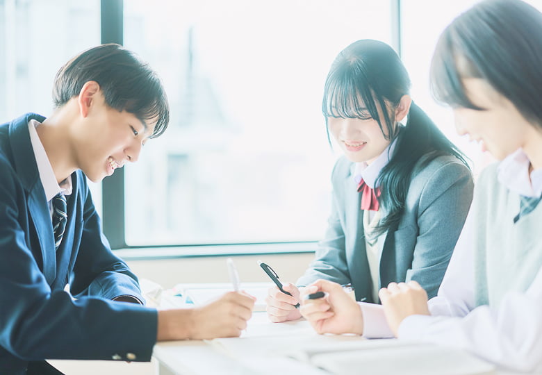 制服を着た学生3人が机を囲んで書き込みをしている様子